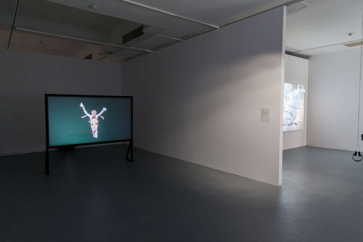 A projector screen sits beside the white gallery walls, on the screen is a person dancing.
