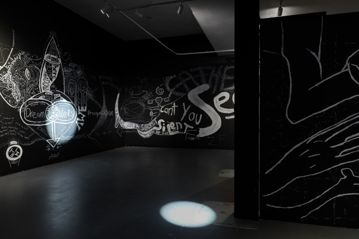Two spotlights highlight the white painted diagrams and words on the black walls in the gallery.