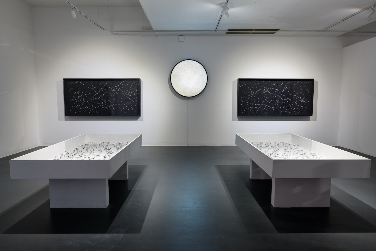 Two white display cabinets sit on the floor; two black display cabinets hang on gallery wall. An orbe shines brightly above and between the cabinets.