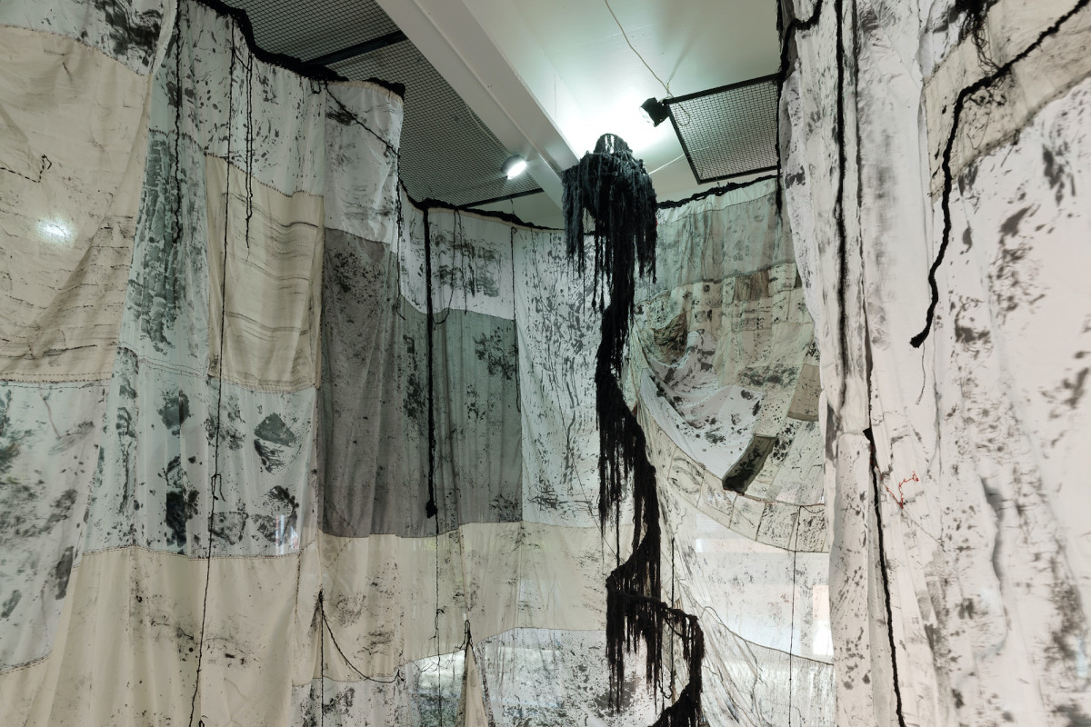 Large textured fabric is draped from the ceiling of gallery.