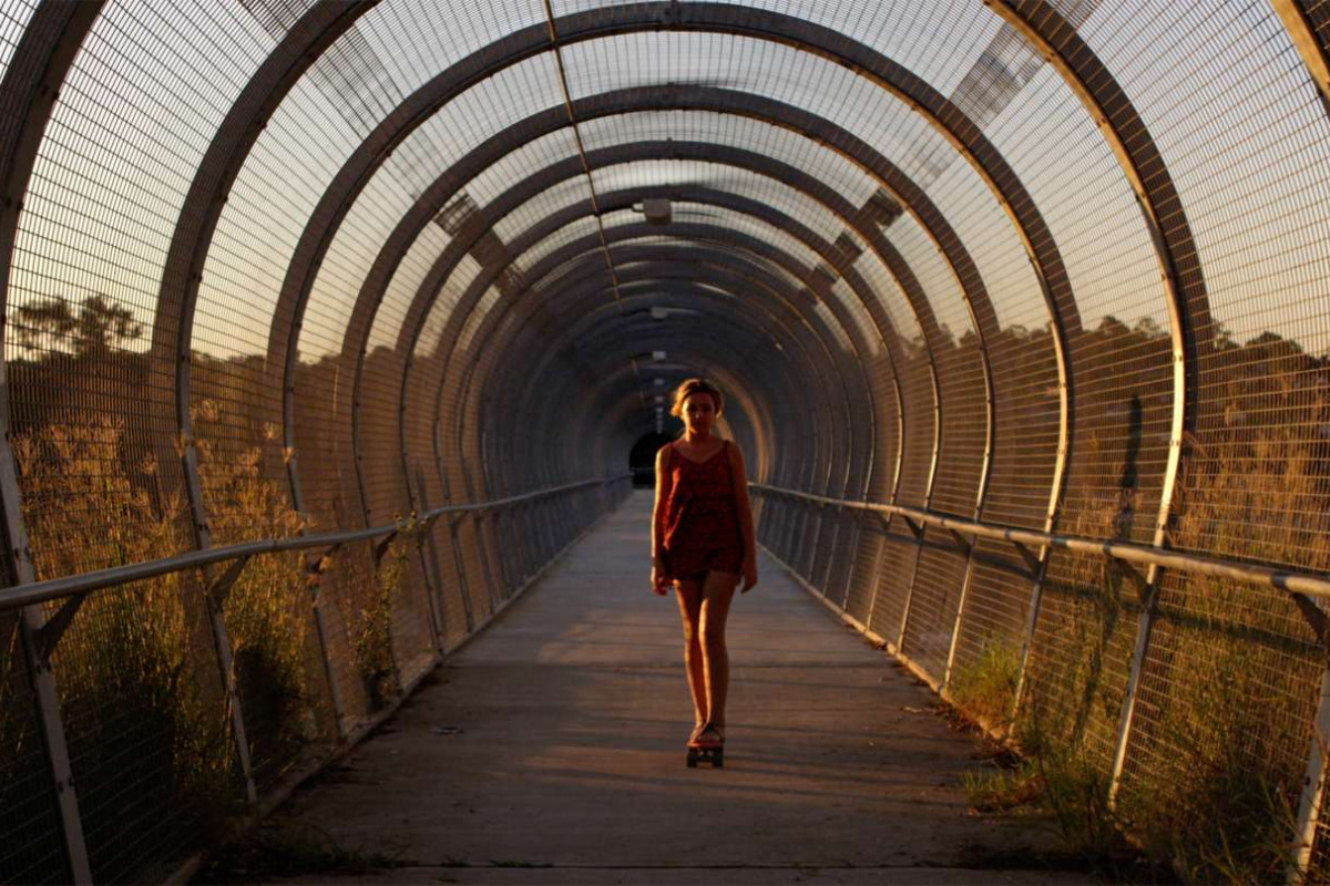A young girl walks through a metal framed bridge tunnel