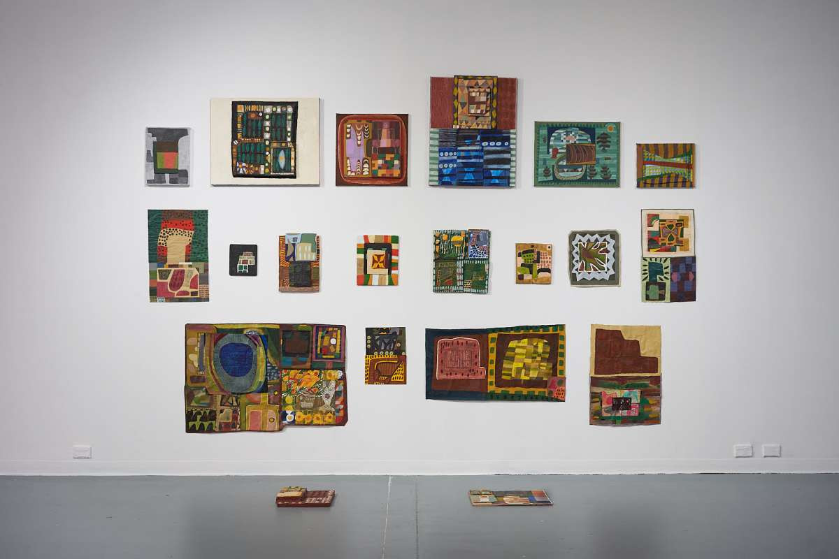A white wall covered in various sized canvases or bright, multicoloured abstract artworks.