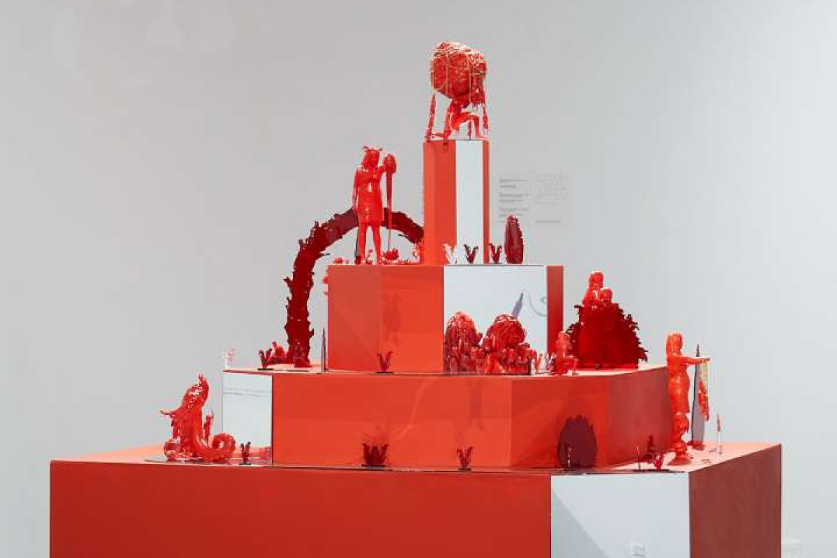A red, tiered plinth is covered in small red figurines of various figures and objects.