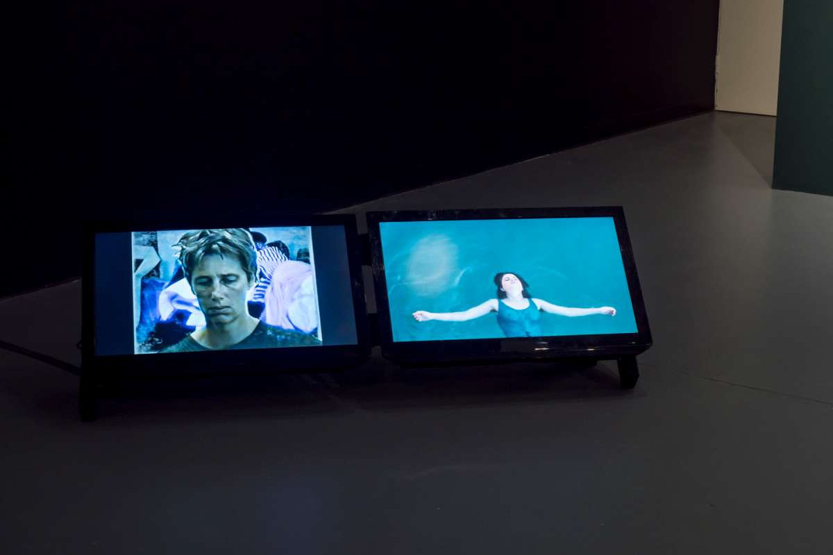 Two digital screens sit side by side, on the left screen a person with short hair looks sad, on the right screen a woman floats in water.