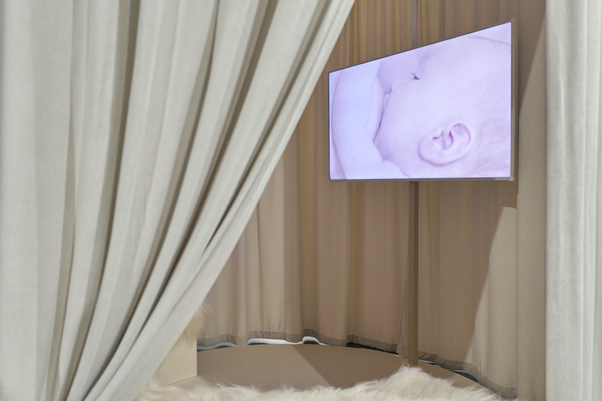 Circular space enclosed with a curtain. A screen within showing a baby being breastfed.