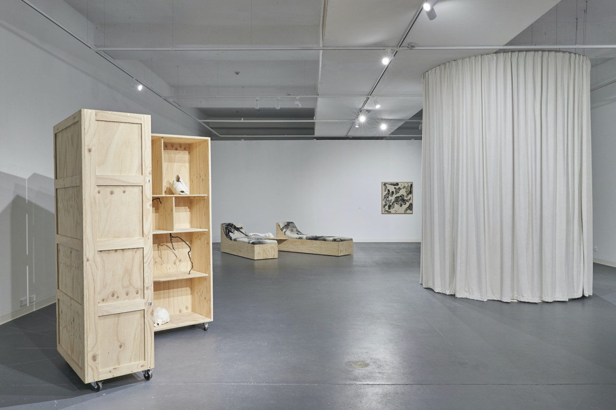 View of the gallery space with the circular curtain to the right, reclined chairs in background and adorned cupboard to the left.