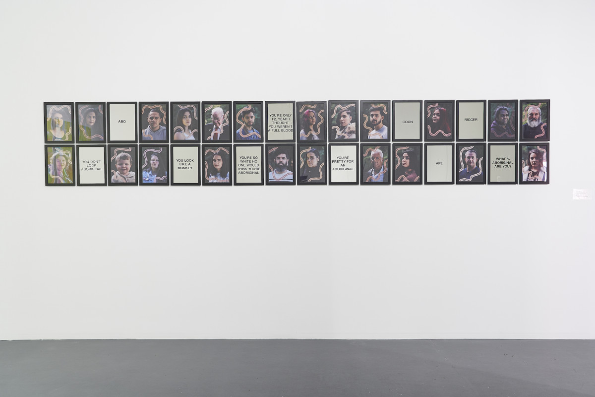 A wall installation comprised of two linear rows of framed portrait images dispersed with framed words.