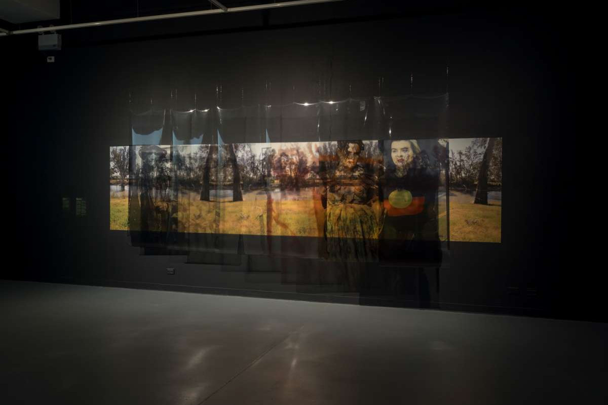 A black wall with a aide image of an outdoor scene, hanging in front of it are sheets of plastic.
