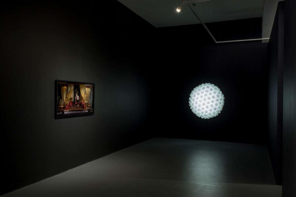 A photograph is framed on a black wall, beside it sits a white lit up sphere.