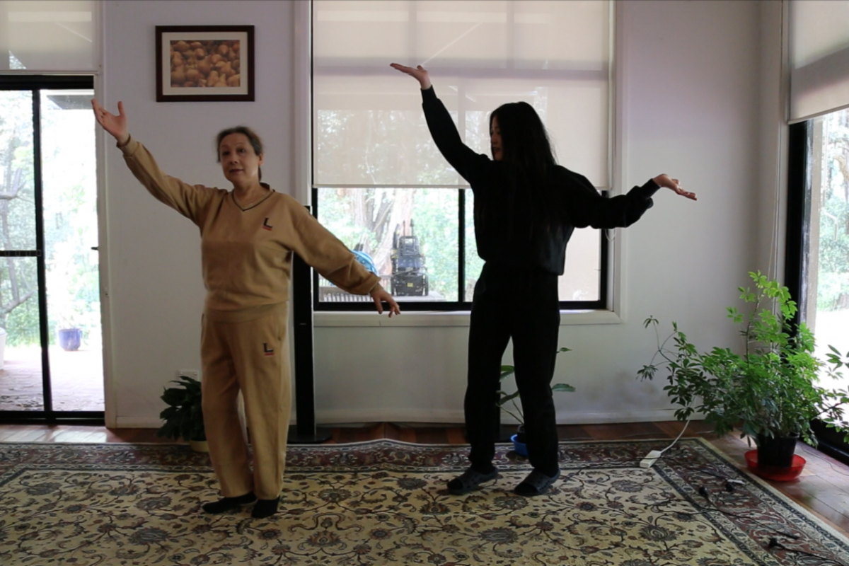Two woman stand side by side with their arms lifted in the same way.