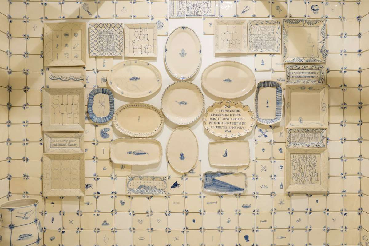 White ceramic tiles with blue drawings on them surround ceramic dishes on a wall.