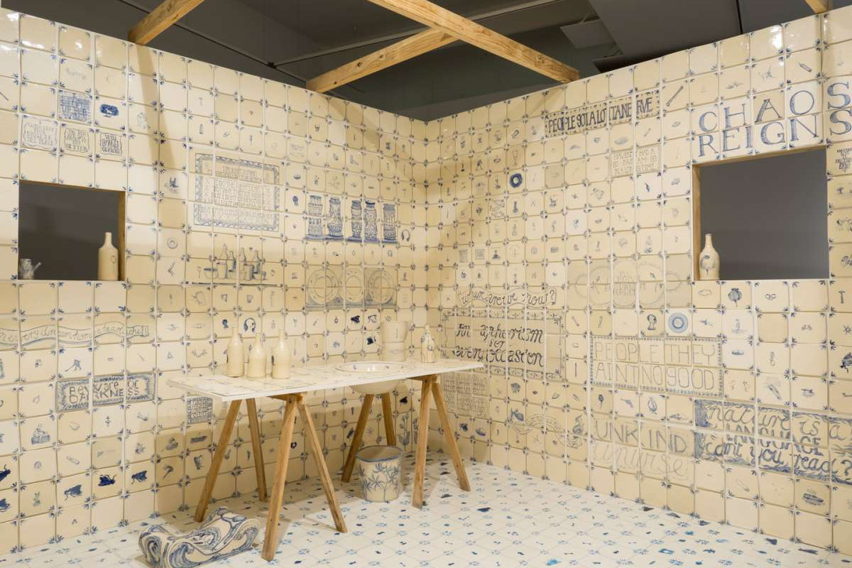 A room tiled from floor to ceiling with white ceramic tiles with blue illustrations and text on them