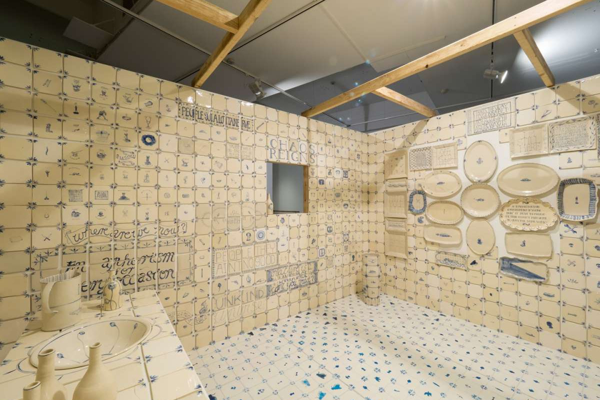 A room fully tiled from floor to ceiling with white tiles with blue drawings and text on them.