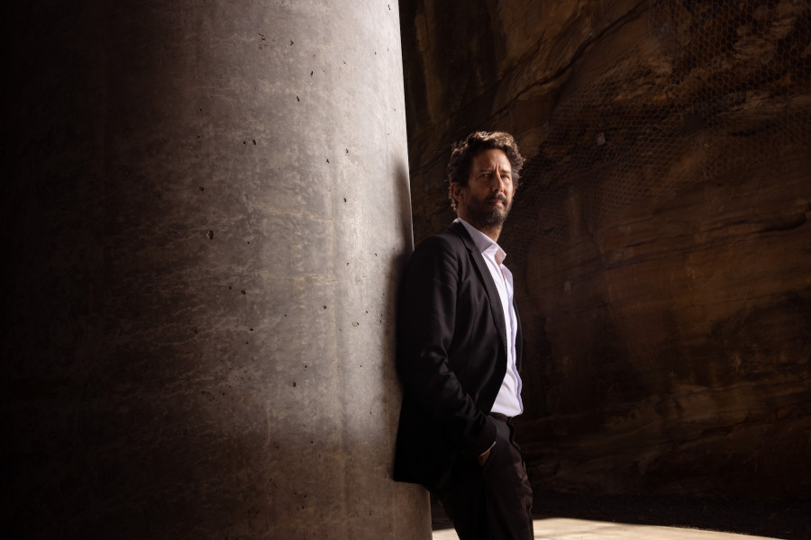 José Roca wears black suit and white shirt, looks off-camera with hands in pockets.