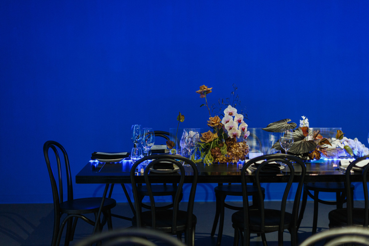 A section of a table, adorned with floral and light installation by Studio Botanic. The wall is blue.
