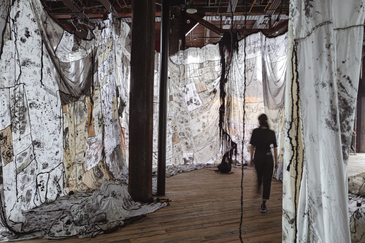 Large textured fabric is draped from the ceiling of a warehouse location.