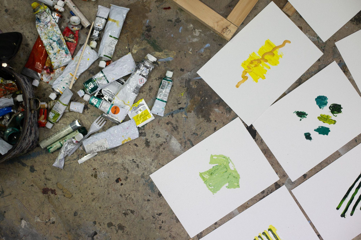 Birds eye view image of paper and paints on the floor. The paper has abstract painted marks.