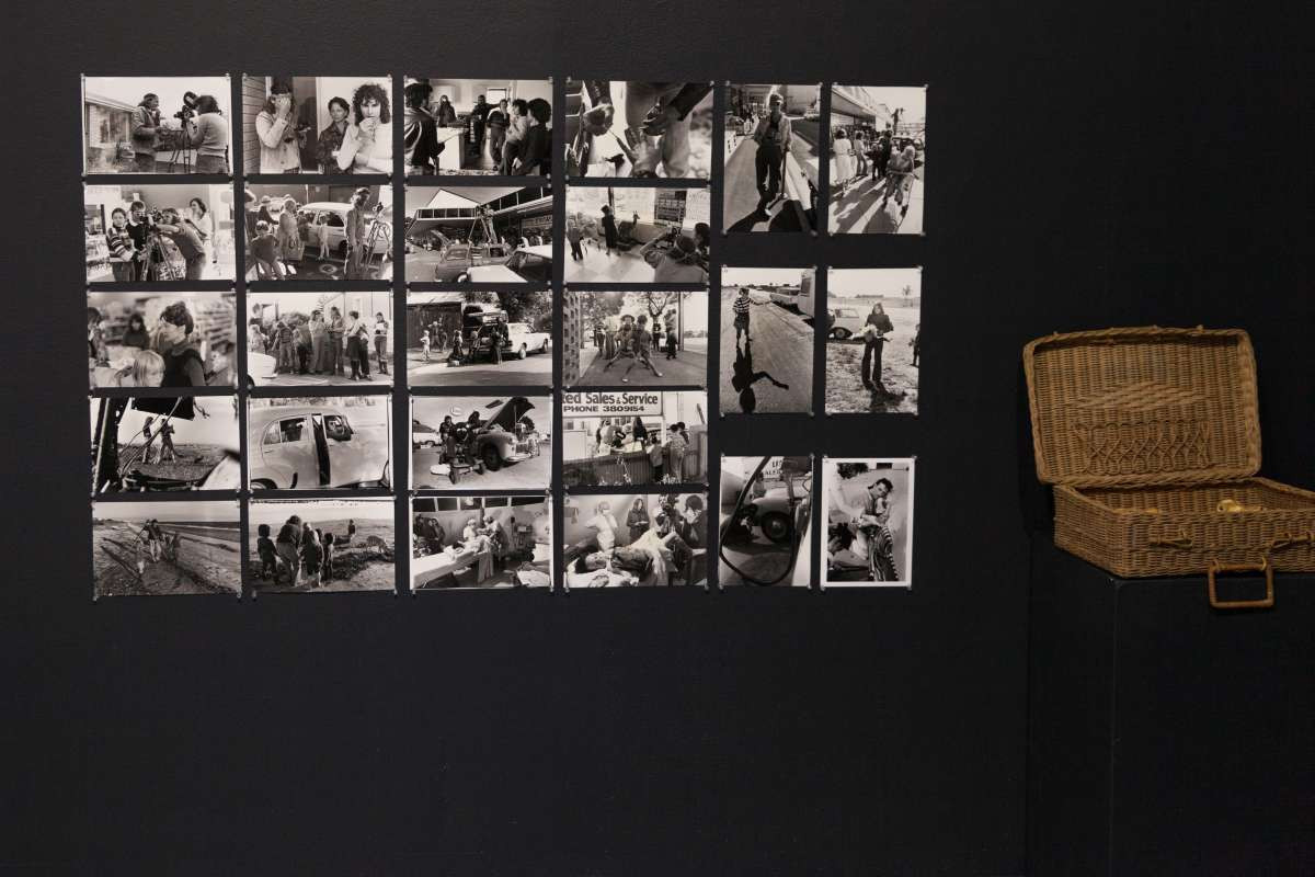 A grid of black and white photographs are pinned to a black wall. Beside them is a rattan basket.