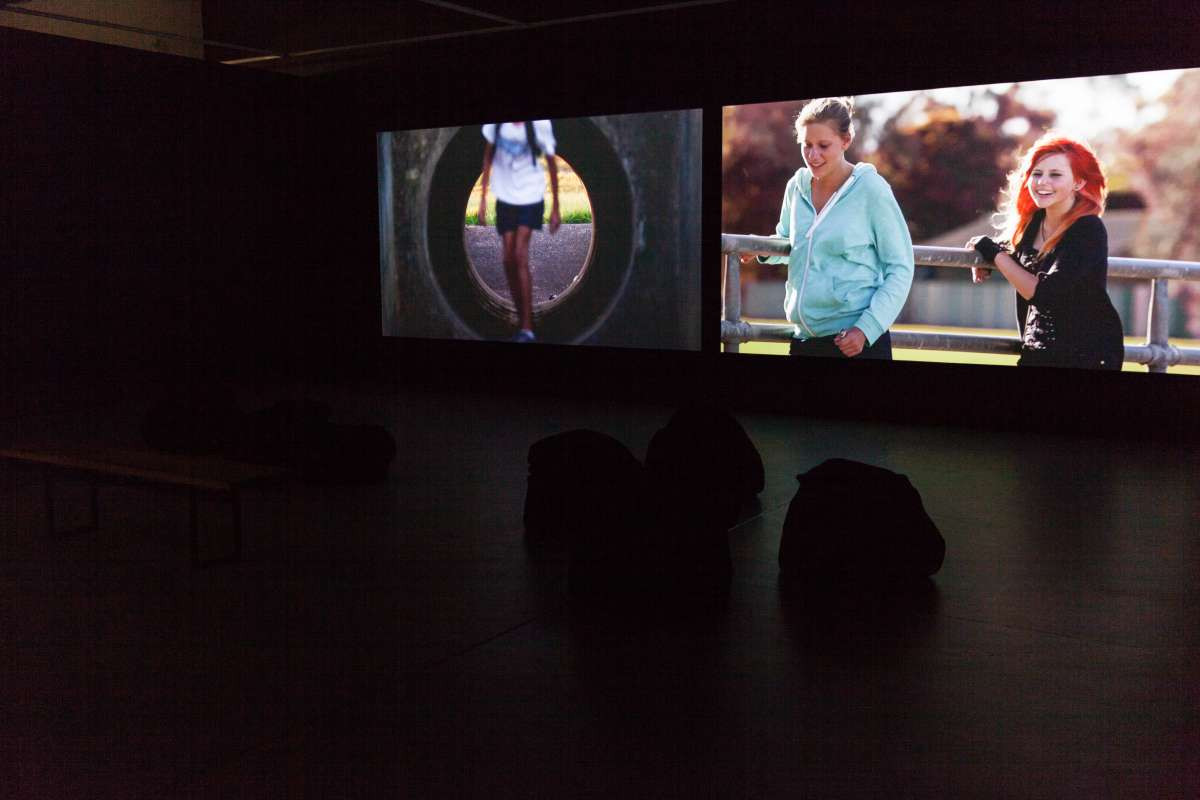 Two projection screens sit side by side, on the screen there are young girls smiling