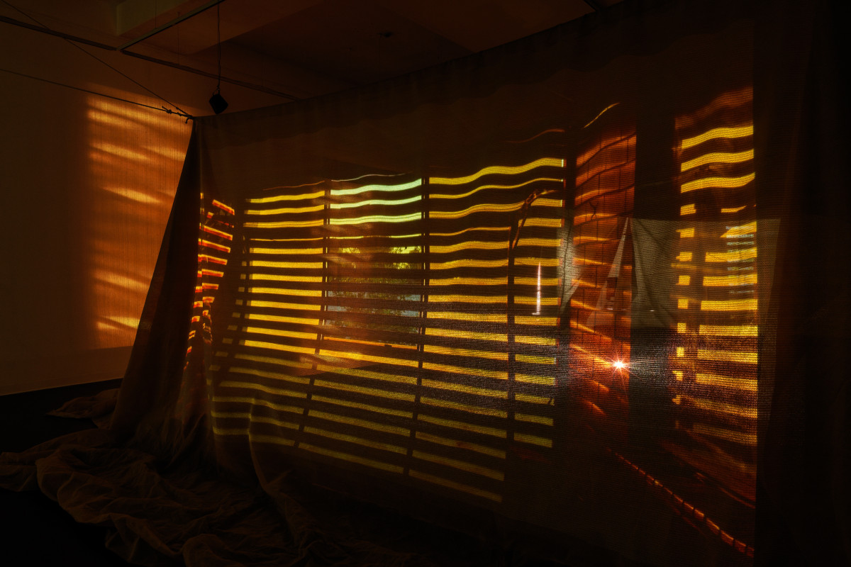 Suspended shade cloth structure in centre of gallery. Projections featuring red shadows spill outward onto the walls from within the structure.