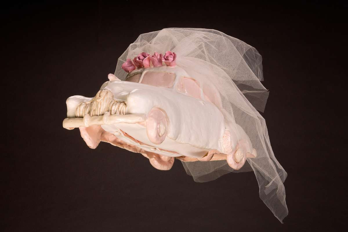 A light pink sculpture of a car, wearing a wedding veil.