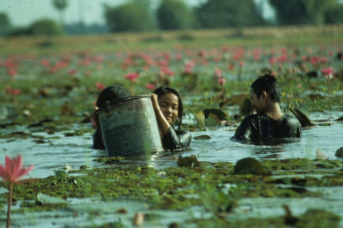 Three smiling young people in a large body of water with a metal bucket.