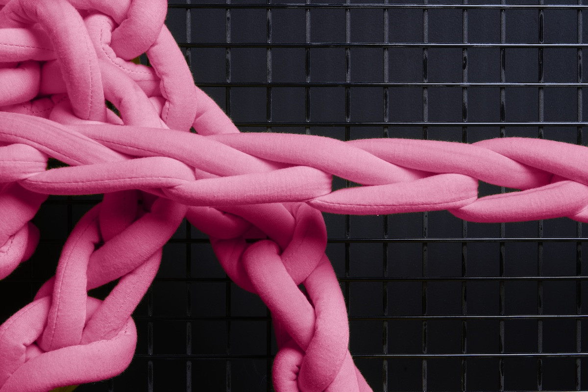 Candy pink stuffed textile chains stretch against a black metal grid background.