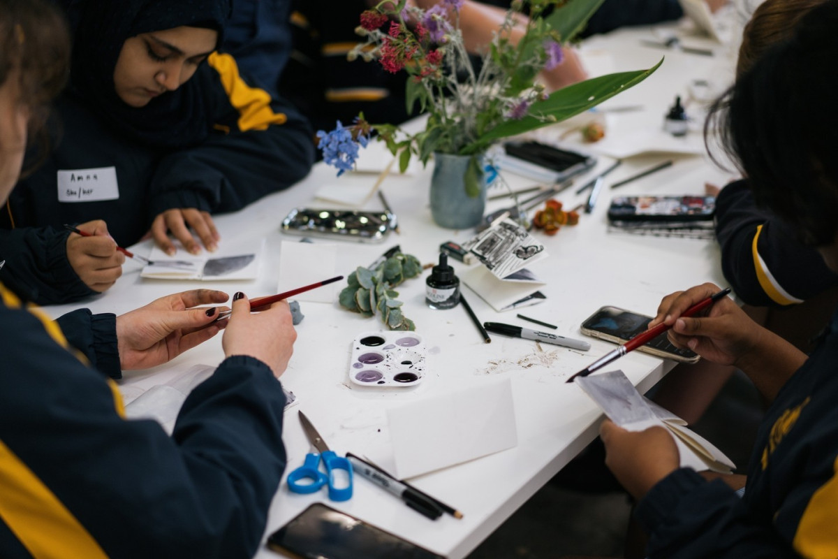 3 students in Asha's workshop gather around the end of a table all painting onto scratchboard.