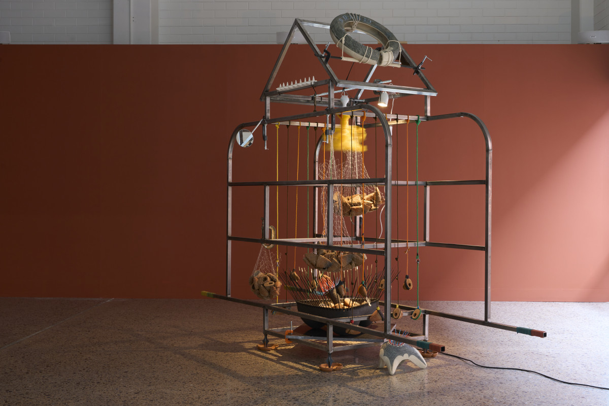 Metal frame artwork resembling a sari-sari store, adorned with ropes, nets, and hanging ceramic objects.