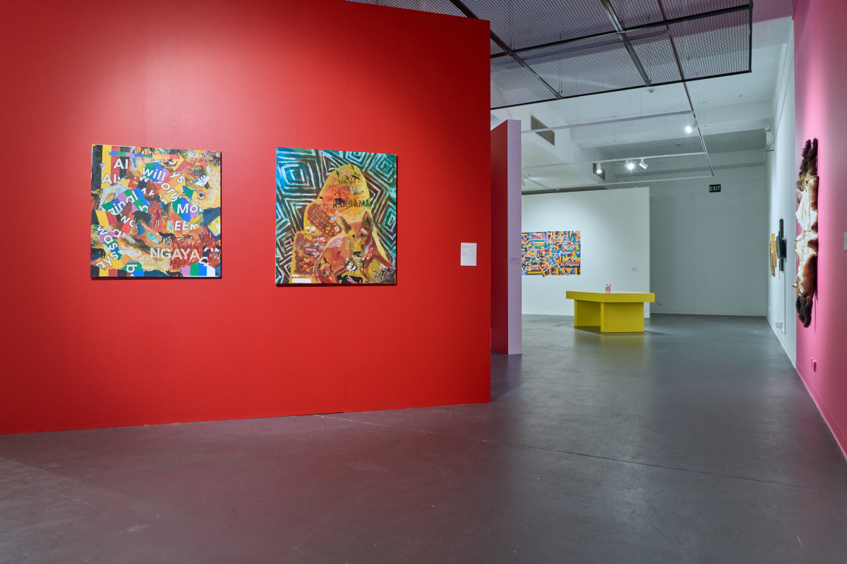 A wide view of the exhibition. Focus is on red wall that features two square hanging works.