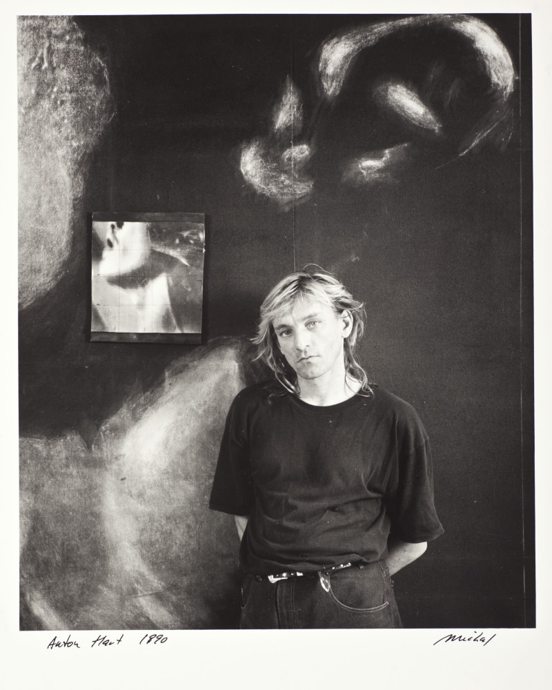 Black and white photograph of Anton Hart looking to camera. He wears black tee shirt and jeans with a belt.