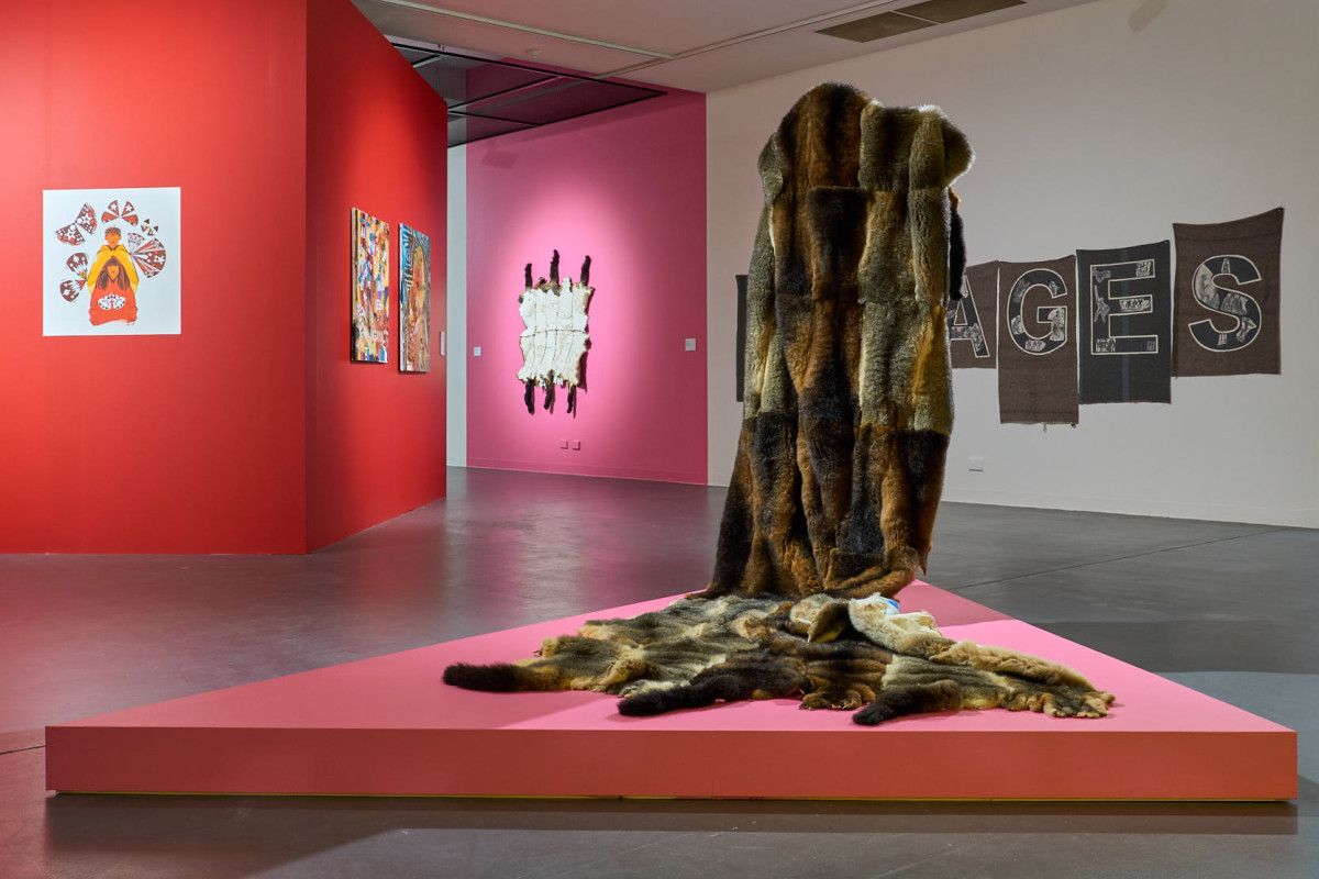 A large cloak made from possum pelts stands on a pink plinth in a gallery.