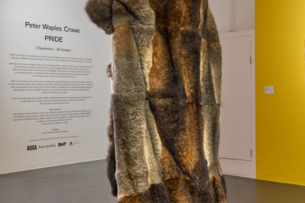 A large cloak made from possum pelts stands on a pink plinth in a gallery.