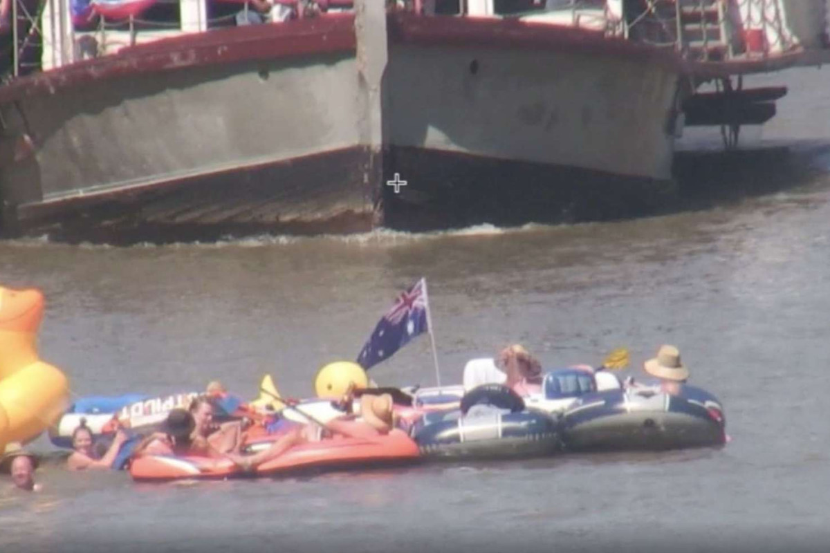 A boat on the Murray River, with a group of people in the water and inflatable rafts in front of it.
