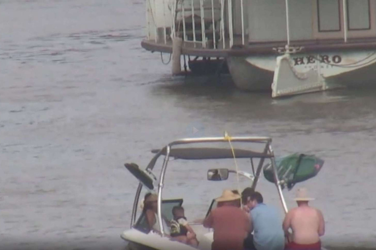 A group of people in a small boat on the river. Their boat faces a larger boat.