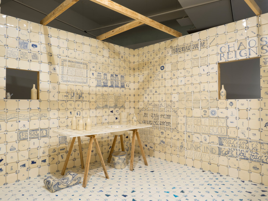 A room tiled from floor to ceiling with white ceramic tiles with blue illustrations and text on them