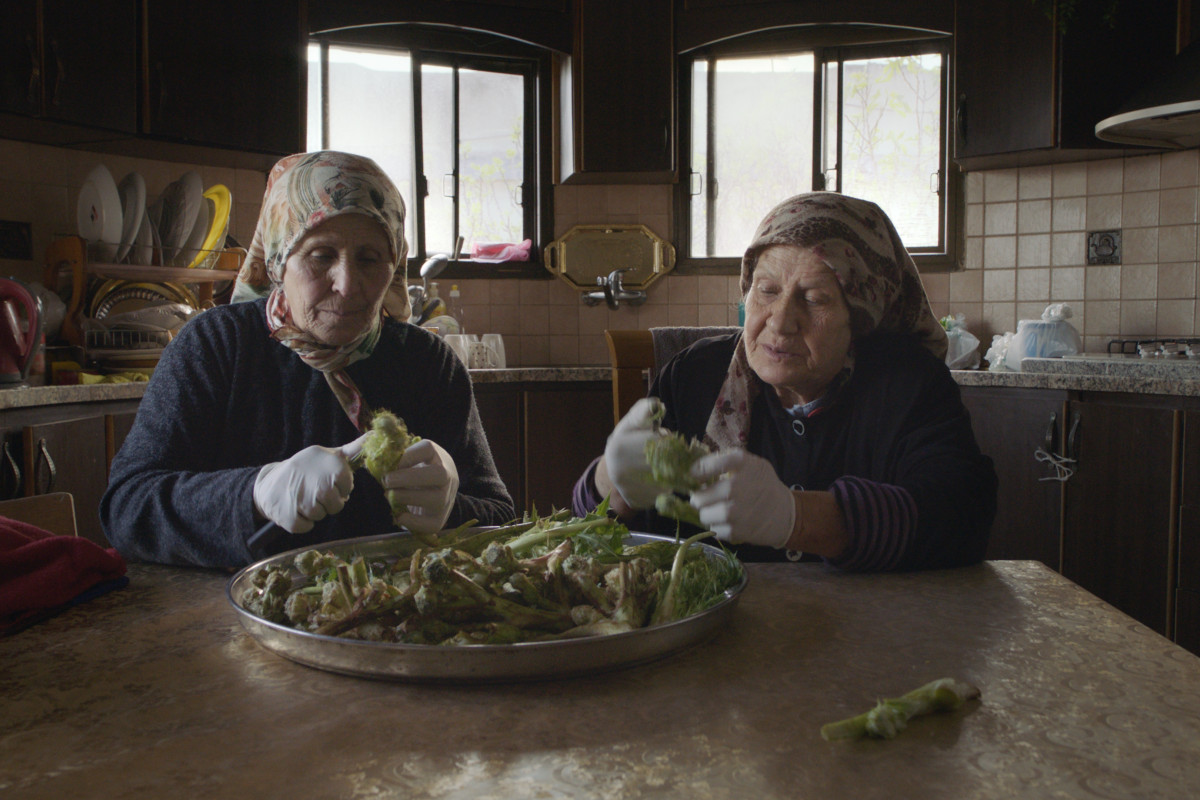 Two older women sitting at a kitchen table preparing vegetables