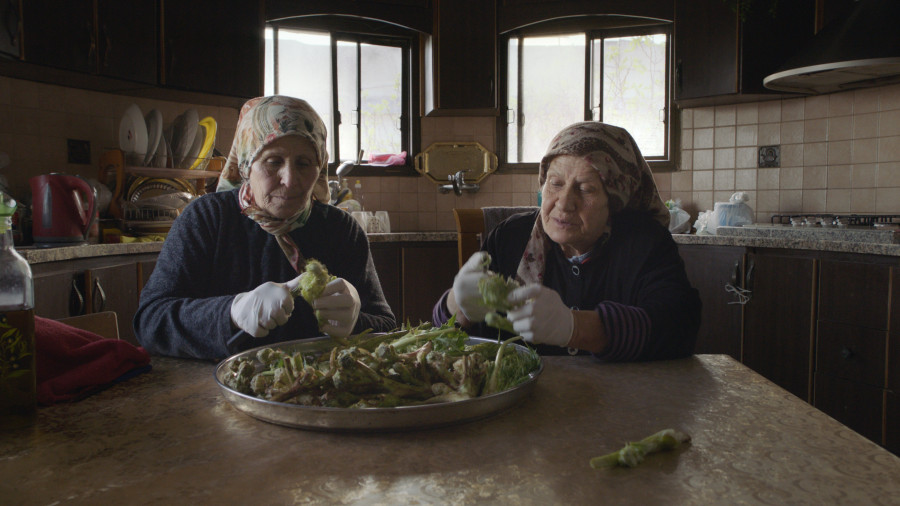 Two older women sitting at a kitchen table preparing vegetables