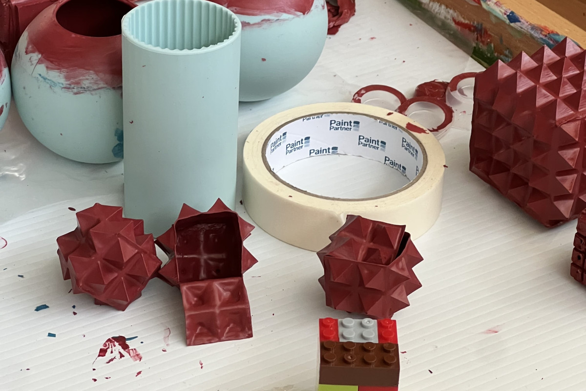 Katey Smoker's ACE Studio desk featuring sphere and cylinder paint moulds, lego pieces, a roll of masking tape and Smoker's red spiked cube artworks made from dried paint.