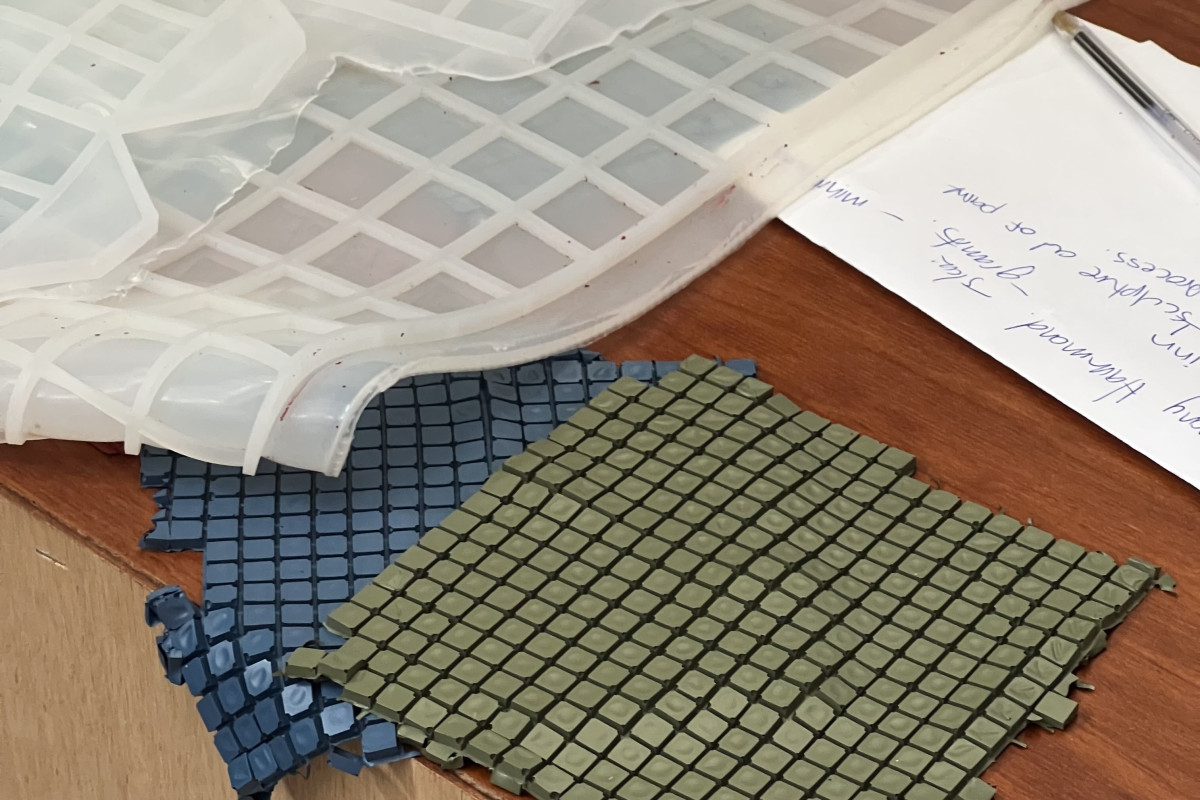 Katey Smoker's ACE Studio desk featuring clear silicon paint moulds and Katey Smoker’s artwork which are sheets of dried paint made into a repetitive square pattern in colours green and blue.