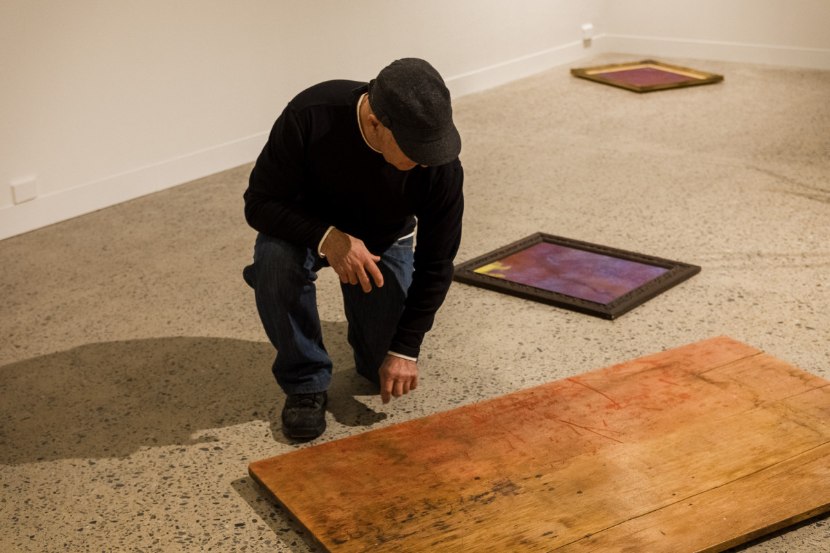 Lee knees on one knee looking at one of his artworks on the gallery floor.