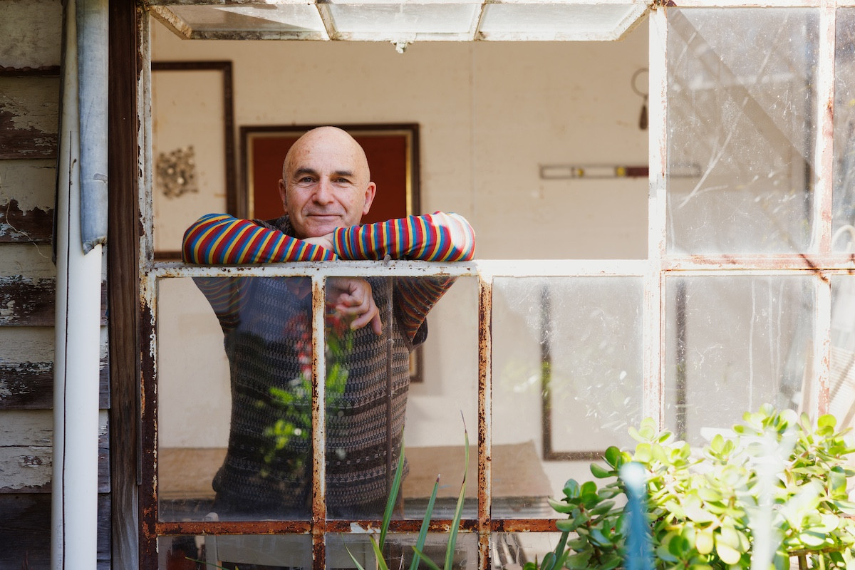 Lee stands in his home studio leaning on an open window looking outward.