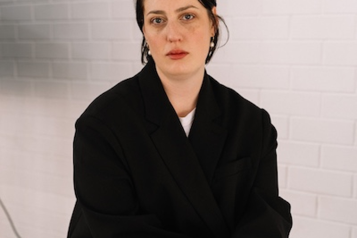 Patrice sits crossed legged facing the camera. She wears a black blazer and blue jeans.