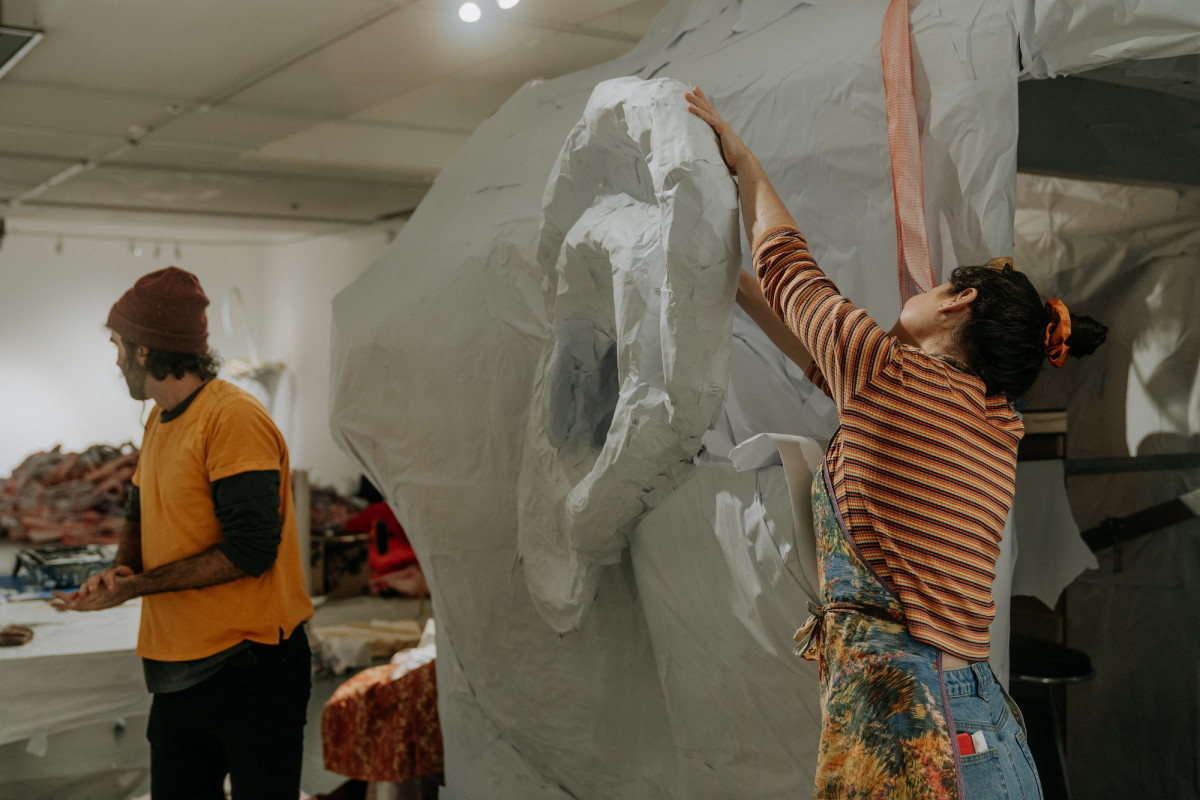 Two helpers working on ROCKAMORA in the papier-mâché stage of the build. Camera focused on an ear.