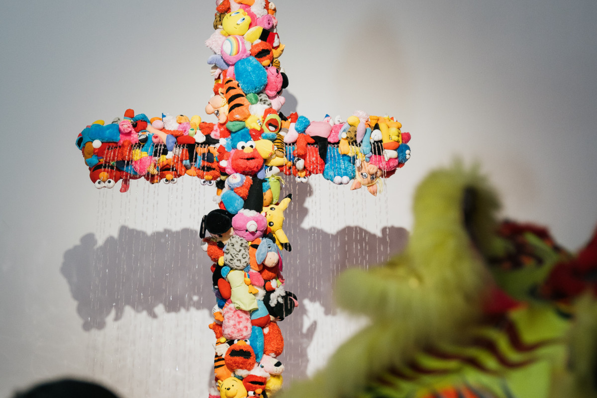 A tall crucifix which is engulfed in an array of dismembered soft toy limbs. Intermittently a water feature, the crucifix is activated producing streams from the crucifix into a pool of toy fish Koi.