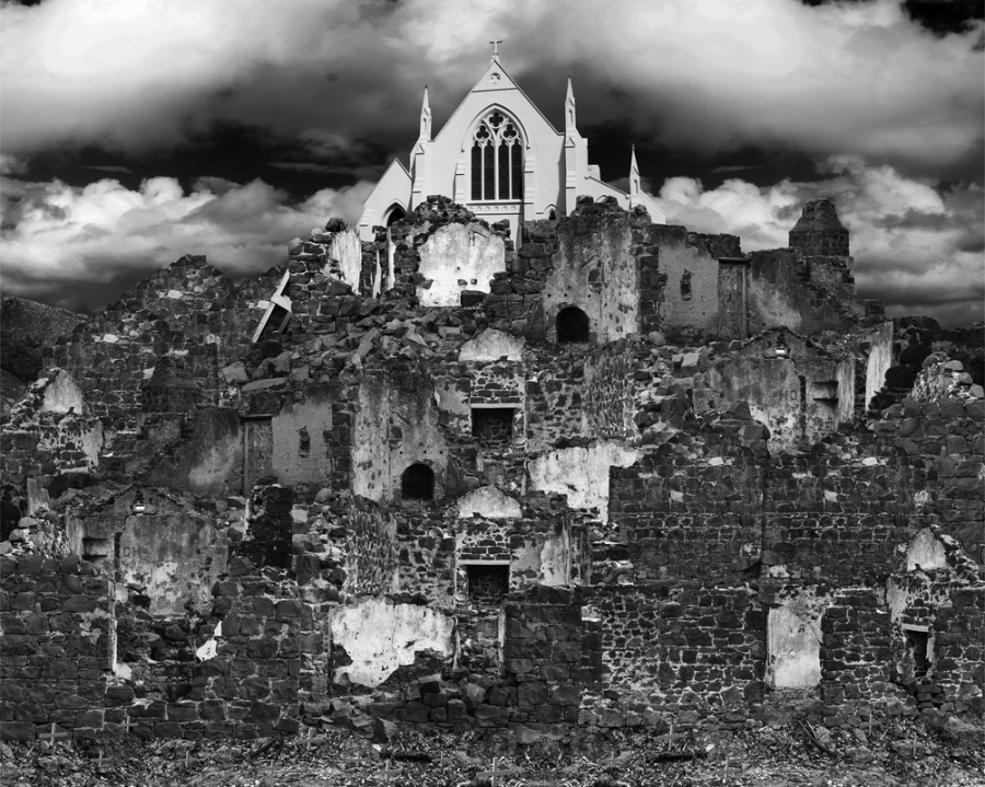 Black and white photographic image of collaged ruins with dramatic clouds with a white church looking over the ruins.