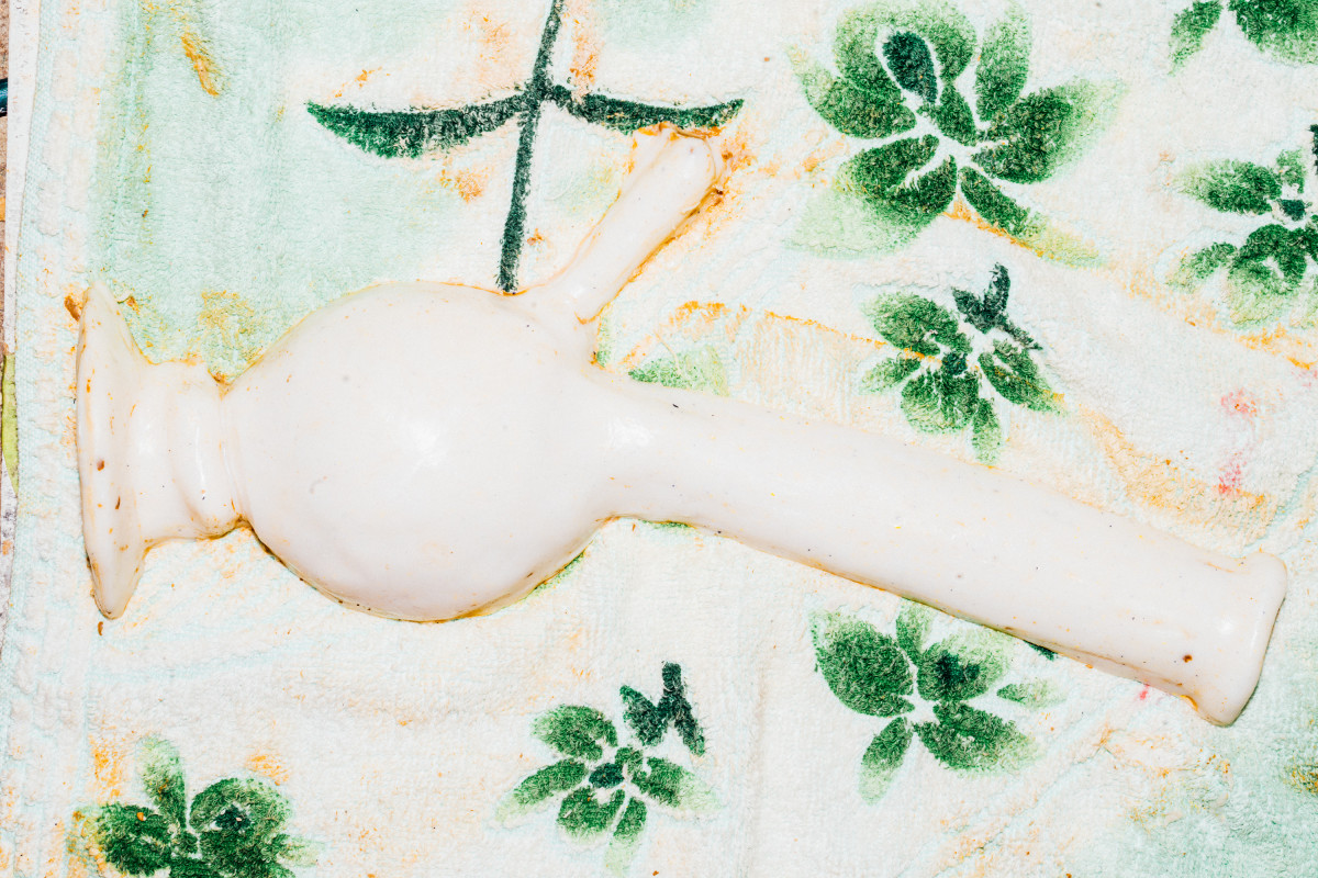 A white soap cast of a bong rests on a green towel with a floral pattern. There is residue of clay marked on the towel and bong.