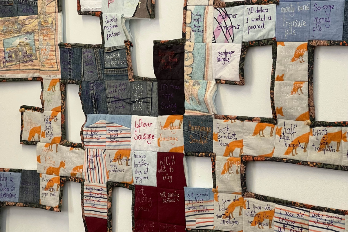 A quilt made of denim and patterned fabric off-cuts embroidered with the artist's google search history.