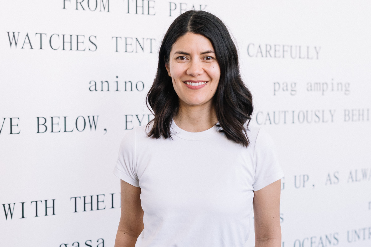 Rayleen Forester smiles to camera with hands in pockets. She stands in front of her work Mother Mountain in the gallery at POP Studios.