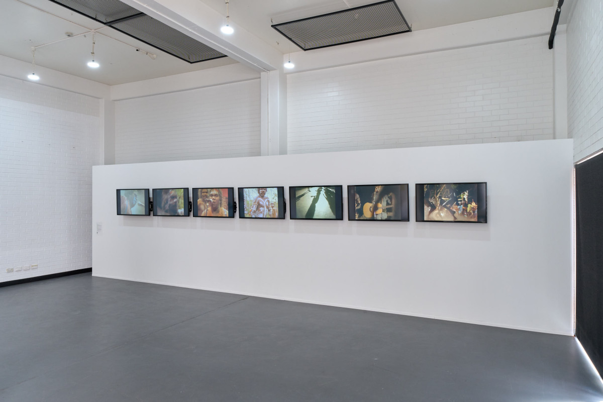 Treaty is a multi-channel video installation across 7 screens. The screens, displayed in a horizontal line, each play the music video for ‘Treaty’ by the band Yothu Yindi.